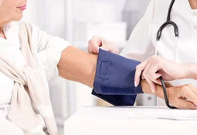 Lächelnde Patientin des Ambu-Teams Düren bekommt am Oberarm den Blutdruck in Form einer Behandlungspflege von einem kompetenten Mitarbeiter gemessen.